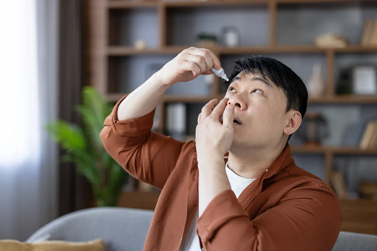 a man putting in eye drops for dry eyes at home