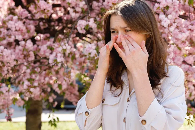 a woman rubbing her eyes outside during spring